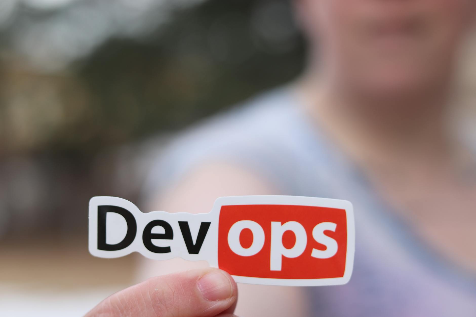 Dłoń trzymająca naklejkę DevOps w otwartej przestrzeni outdoors