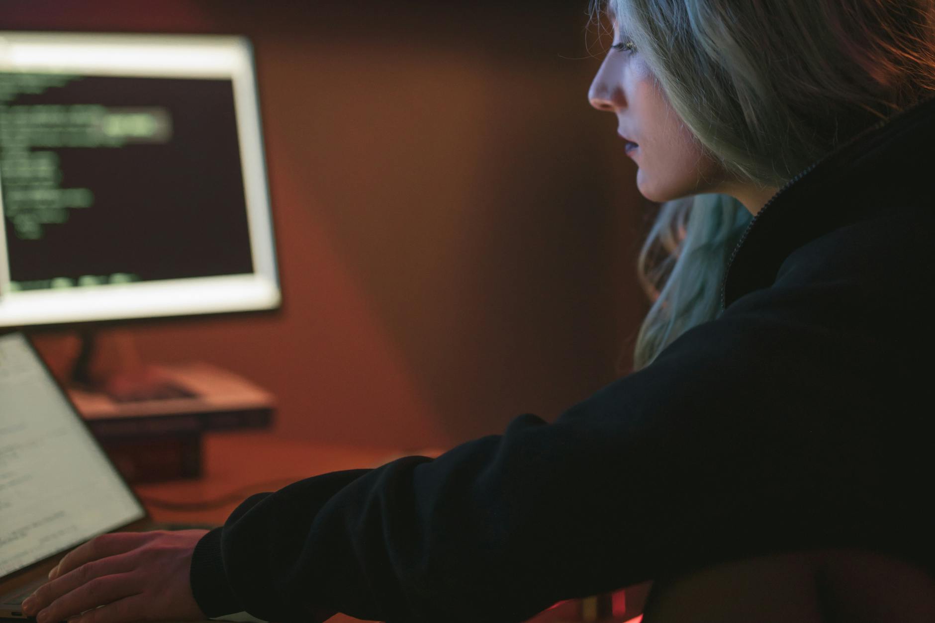 Kobieta pracuje nocą przy laptopie z kodem w ciemnym pokoju