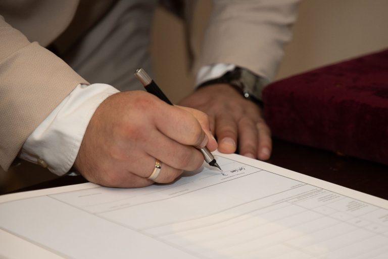 Mężczyzna z obrączką podpisujący dokument długopisem